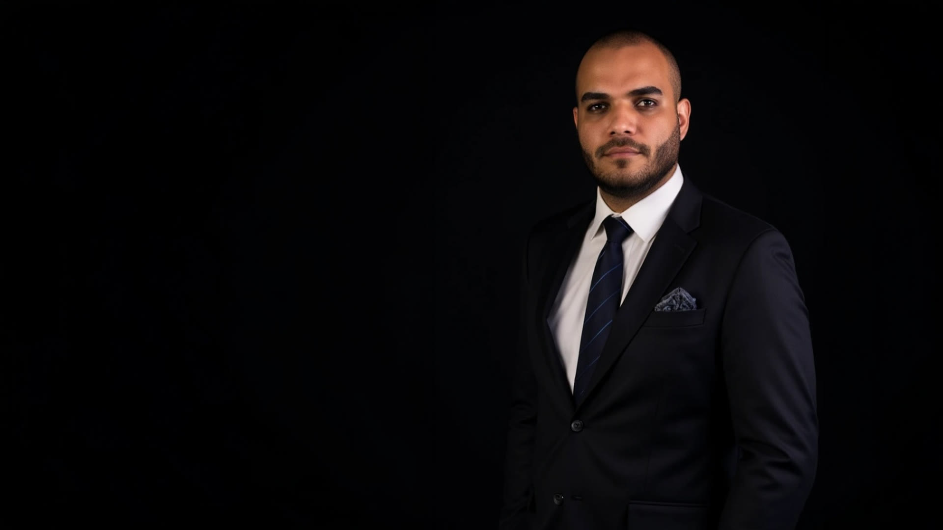 Breno Amâncio de terno preto em fundo escuro
